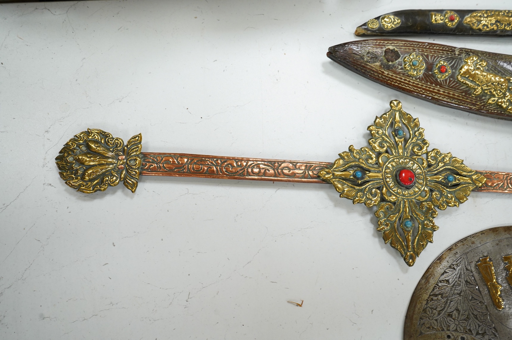 A decorative Indian axe, the large head inlaid with brass Hindu figures, together with a brass mounted North Indian kukri, another similar knife with bone handle, and a large shovel-shaped copper and brass item possibly